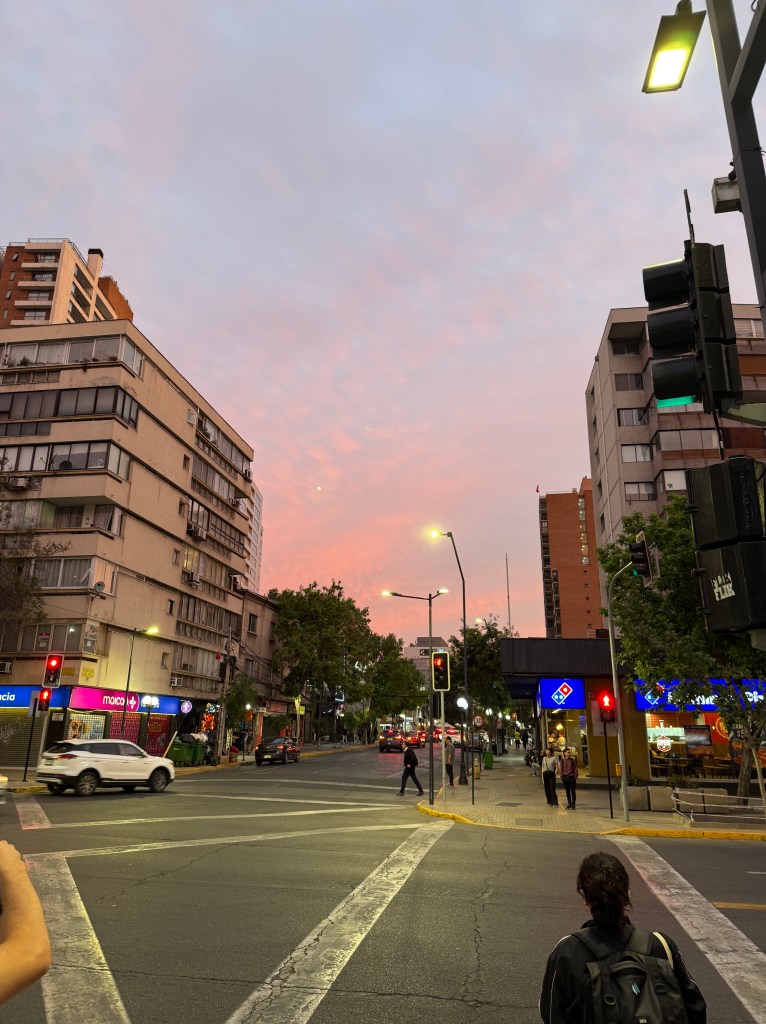 A vibrant sunset over a busy street in Santiago, Chile, showcasing buildings, traffic lights, and pedestrians.