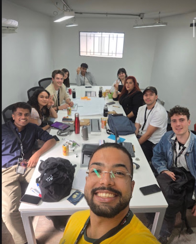 Group of international students collaborating in a conference room, smiling and working together at a table with various materials and electronic devices.